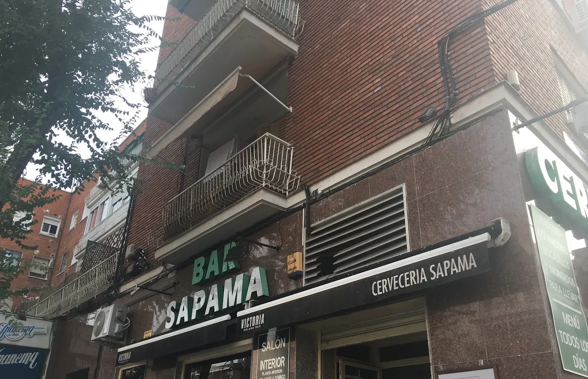 Fachada de Bar Sapama de día, en la esquina, con el rótulo verde y blanco, el toldo de Cervecería Sapama y el cartel del salón interior
