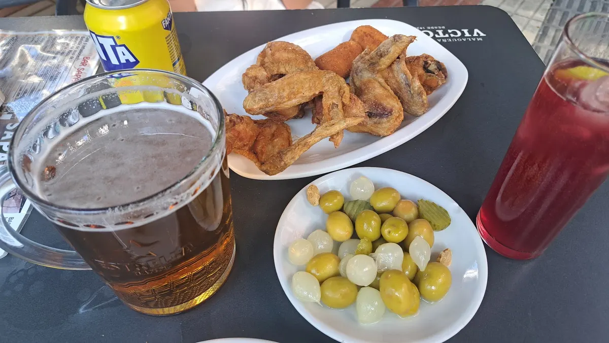Jarra de cerveza, un tinto con limón, alitas y un plato de aceitunas y cebolletas en una mesa de la terraza