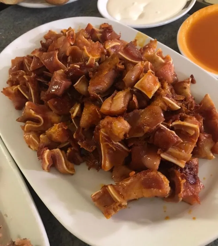 Ración de oreja a la plancha en trozos dorados, con un cuenco de salsa al lado